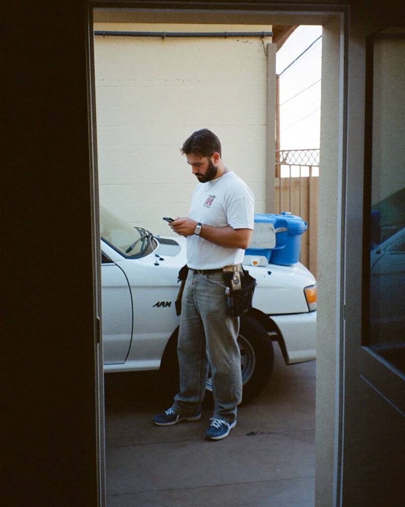 An American plumber in his 40s standing by his work truck, reading an emailed proposal on his phone.